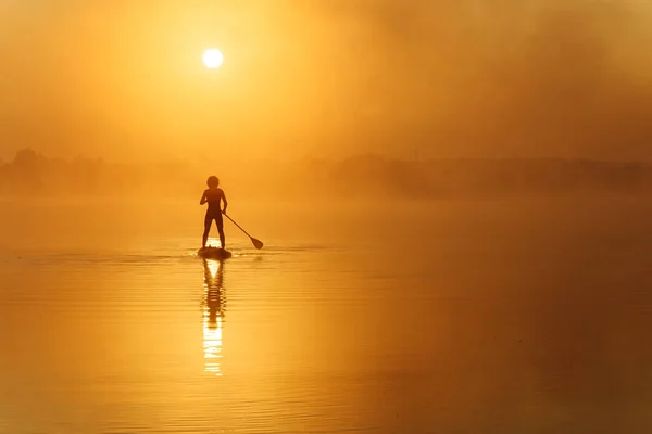 Jovem praticando em sup boarding durante o horário da manhã — Fotografia de Stock