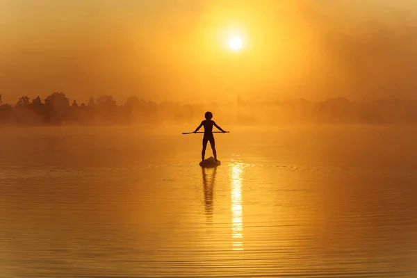 Homem em silhueta flutuando em prancha durante o nascer do sol — Fotografia de Stock