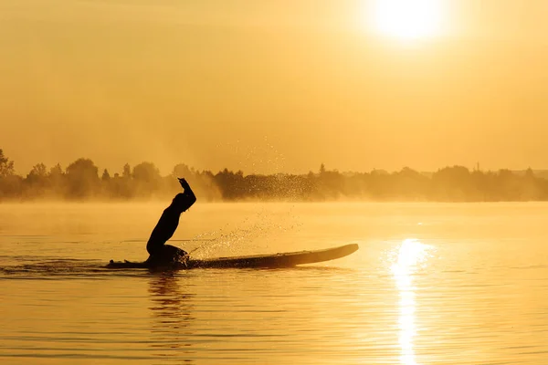 Surfista masculino salpicando água enquanto sentado na prancha de remo — Fotografia de Stock