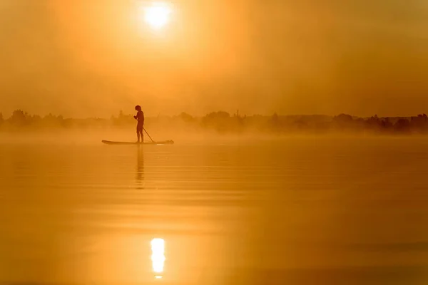 Jovem usando prancha de remo para nadar no lago — Fotografia de Stock