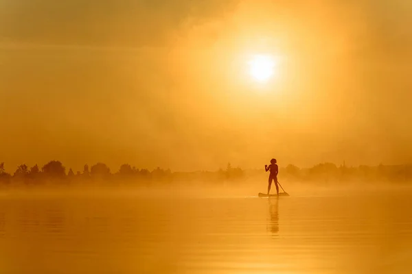 Esportista remando com prancha de remo durante o nascer do sol — Fotografia de Stock