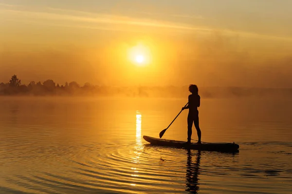 Jovem fazendo surf na prancha de jantar durante o nascer do sol — Fotografia de Stock