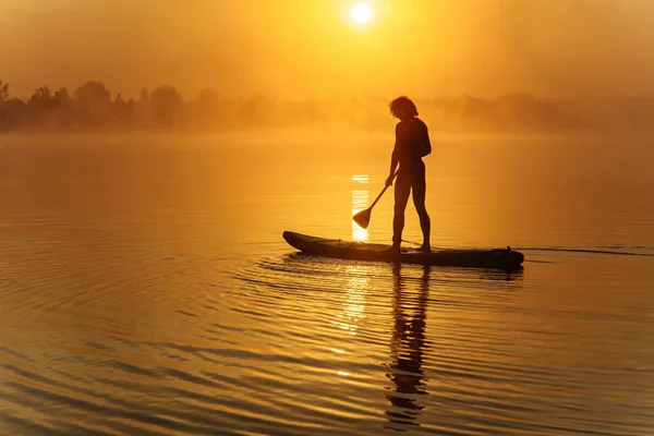 Silhueta de homem atlético remando a bordo em lago nebuloso — Fotografia de Stock