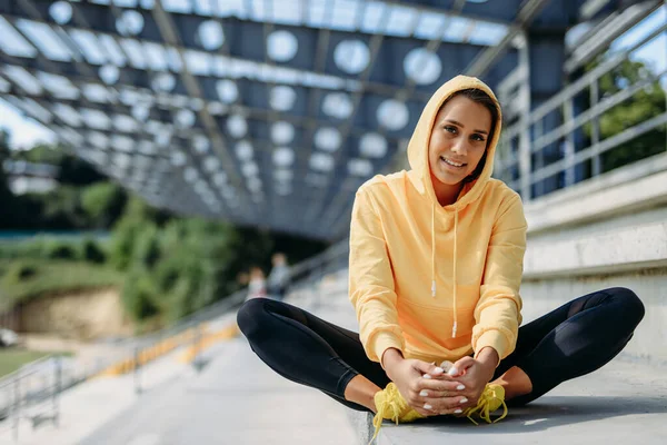 Sportive woman in yellow hoodie warming up on stairs