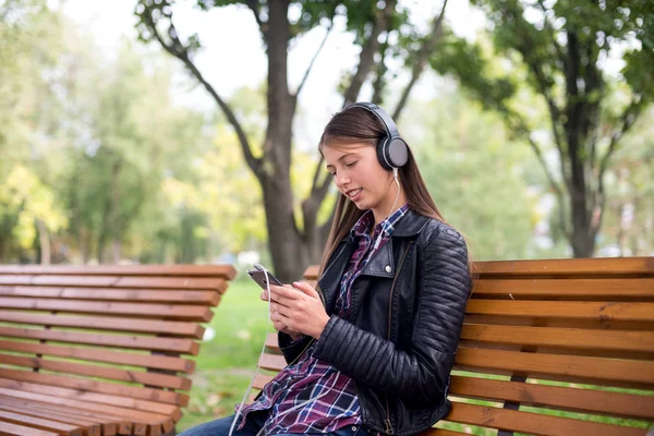 Woman listening to music. Female student girl outside in park listening to music on headphones. Happy young university student of mixed Asian and Caucasian ethnicity.