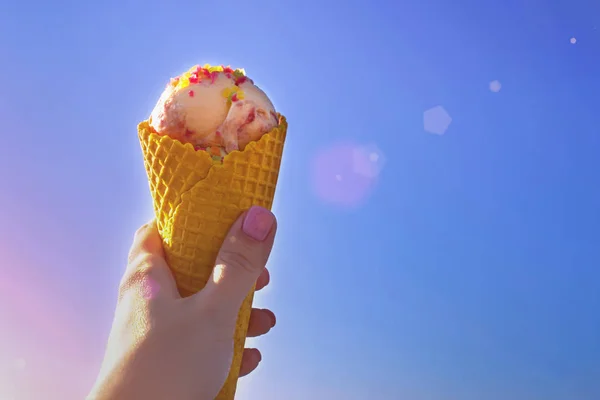 Sorvete rosa em um chifre amarelo contra o céu azul na mão — Fotografia de Stock