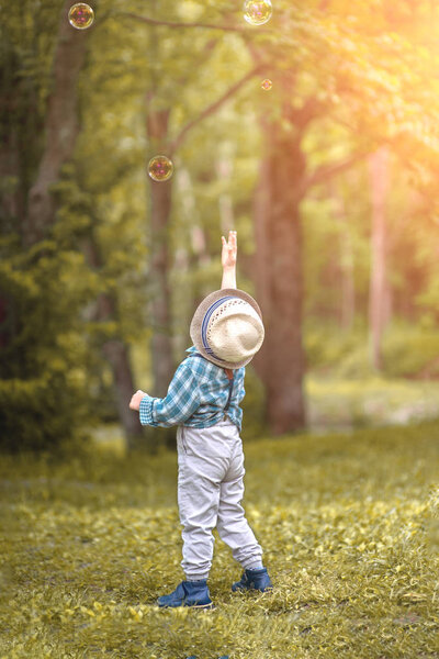a little boy in a hat reaches for soap bubbles