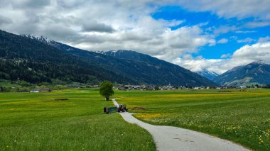 Innsbruck yakınlarındaki dağ vadisinde tarım işi. Ön planda bir traktör var, arka planda kilisesiyle birlikte Avusturya köyü..