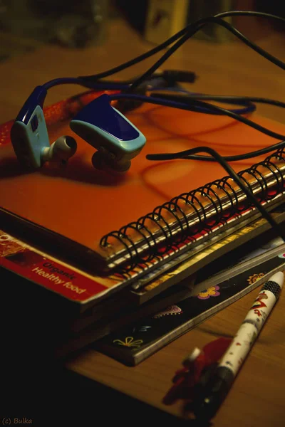 Um caderno e uma caneta estão em uma mesa de casa sob uma lâmpada. O conforto de uma bagunça doméstica . — Fotografia de Stock