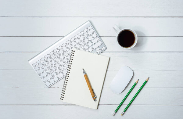 Wooden White office desk table with cup of coffee, Notebook, Pen, Computer Keyboard Mouse on it. Top view with copy space