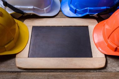 Sarı, turuncu, beyaz ve mavi koruyucu güvenlik kask ile eski ahşap arka plan kara tahta. Emanet ilk kavramlar