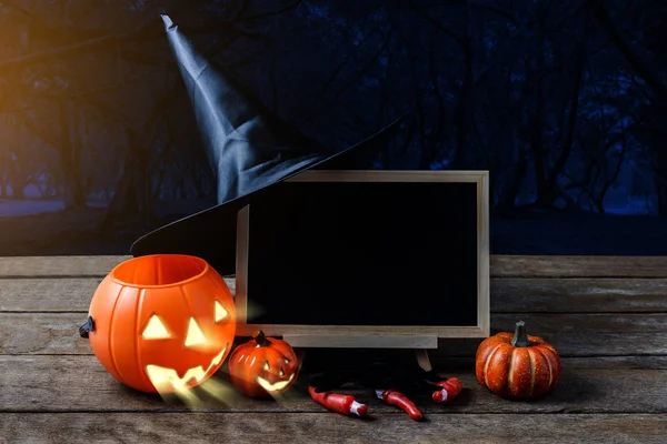 Halloween background. Spooky pumpkin, Witch hat, Black spider, chalkboard on wooden floor with moon and dark forest. Halloween design with copyspace