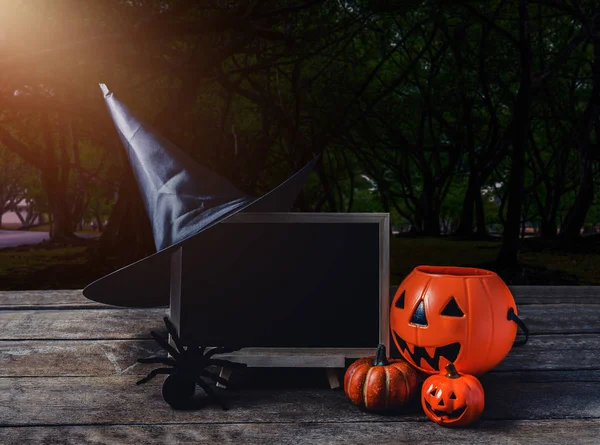 Halloween background. Spooky pumpkin, Witch hat, Black spider, chalkboard on wooden floor with moon and dark forest. Halloween design with copyspace