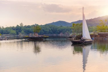 Yelkenli büyük bir rezervuar içinde arka plan olarak dağlar var. Günbatımı zamanı