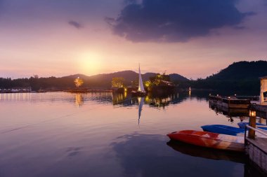 Yelkenli büyük bir rezervuar içinde arka plan olarak dağlar var. Günbatımı zamanı