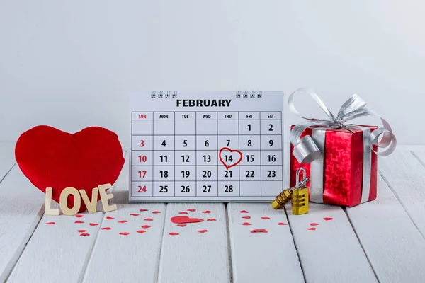 Calendar page with red hand written heart highlight on February 14 of Saint Valentines day with Couple Combination golden padlock and red Heart shape, Gift box, Wooden letters word \