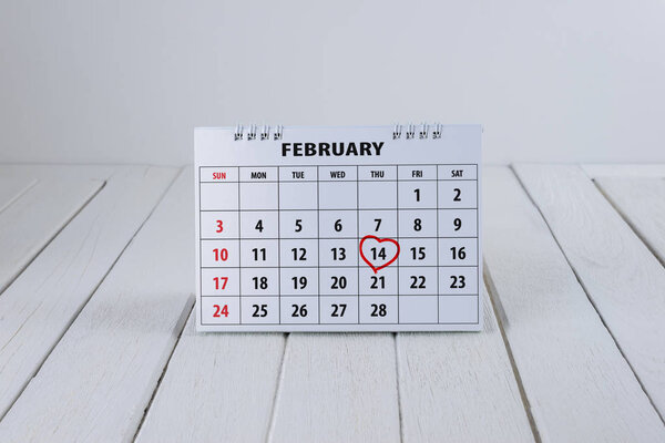 Страница календаря с красной рукописной надписью "Сердце" на белом деревянном столе с пустым местом для текста 14 февраля в день Святого Валентина

