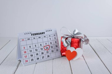 Takvim sayfası ile kırmızı el kalp vurgulamak kırmızı hediye kutusu ve beyaz ahşap masa üzerinde kalp şekli ile Saint Sevgililer günü 14 Şubat tarihinde yazılı
