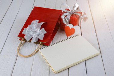 Boş defter ve kırmızı hediye çanta, kutu beyaz ahşap masa üzerinde kalp şeklinde. Saint Sevgililer günü kavramı