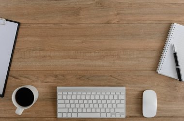 Düz yatıyordu, ahşap ofis masasının üstünde. Çalışma alanı boş pano, fare bilgisayar, klavye, kalem, kahve fincanı ofis malzemesi ahşap masa arkaplanlı.