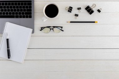 Düz yatıyordu, ahşap ofis masasının üstünde. Çalışma alanı boş pano, dizüstü bilgisayar, fare bilgisayarı, akıllı telefon, gözlük, kahve fincanı ofis malzemeleri beyaz ahşap masa zemininde coppy alanı