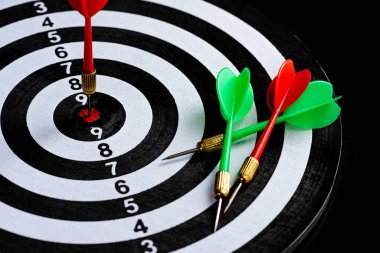 Hedef merkezdeki Dart tahtasını vuran kırmızı ve yeşil oklar siyah zemin üzerinde izole edilmiş, hedef hedefleme kavramını belirleyen iş hedeflerine meydan okuyan ve hedefe ve pazarlama kavramına erişmeye hazır