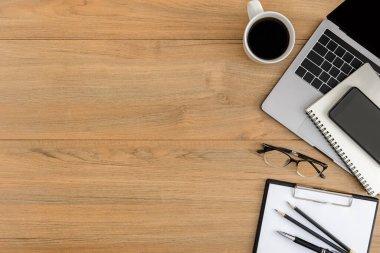 Düz yatıyordu, ahşap ofis masasının üstünde. Çalışma alanı boş pano, dizüstü bilgisayar, akıllı telefon, kalem, kahve fincanı ofis malzemesi ahşap masa arkaplanlı.