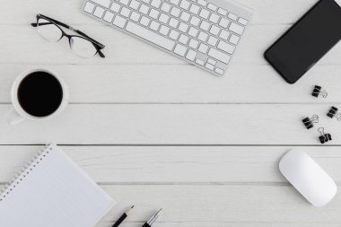 Düz yatıyordu, ahşap ofis masasının üstünde. Çalışma alanı boş pano, klavye, fare bilgisayarı, akıllı telefon, gözlük, kahve fincanı ofis malzemeleri beyaz ahşap masa zemininde coppy alanı
