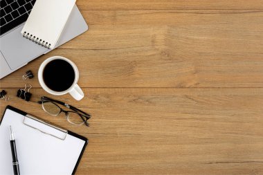 Düz yatıyordu, ahşap ofis masasının üstünde. Çalışma alanı boş dosya, dizüstü bilgisayar, kalem, gözlük, metal şarjör, kahve fincanı ofis malzemeleri ve ahşap masa arkaplanı.