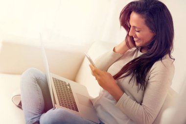 Bir kanepede oturan telefon ile sohbet ederken dizüstü bilgisayar kullanan gülümseyen kadın portresi 