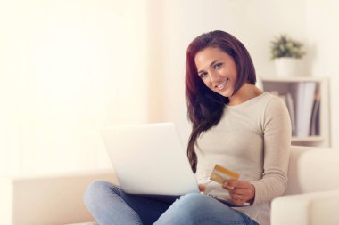 Dizüstü bilgisayar kullanarak ve evde bir kanepede kredi kartıyla online satın alma mutlu kadın portresi