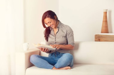 Evde bir kanepede oturan bir kitap okuma gülümseyen kadın portresi