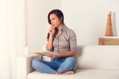 Dalgın kadın evde bir kanepede oturan bir kitap okuma portresi