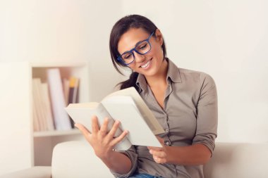 Evde bir kanepede oturan bir kitap okuma gülümseyen kadın portresi