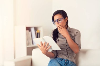 Şaşırmış gibi kadın evde bir kanepede oturan bir kitap okuma portresi