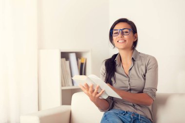 Evde bir kanepede oturan bir kitap okuma gülümseyen kadın portresi