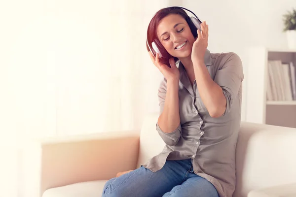 ソファの上にヘッドフォンで音楽を聴く喜びの女性の肖像画 — ストック写真