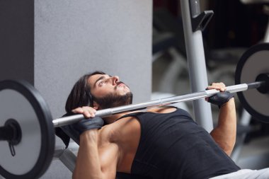 Halterci veya vücut geliştirmeci bir sağlıklı aktif yaşam tarzı ve fitness kavram eğitimi sırasında bir spor salonunda bir halter ağırlık kaldırma bir Bank üzerinde yalan