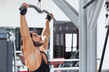 Uygun yetişkin vücut geliştirmeci çekerek bar kırmızı minder koltukta otururken halter makineye kablo ile bağlı