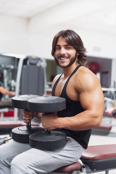 Bodybuilder Der Einem Fitnessstudio Auf Einer Bank Sitzt Hantelgewichte Hebt — Stockfoto