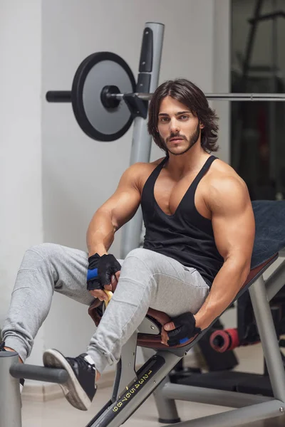Portrait of young adult Bodybuilder sitting on a barbell weight bench in a gym and looking at camera