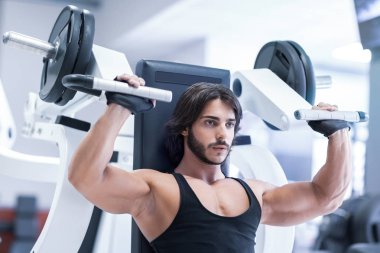 Bir sağlıklı aktif yaşam tarzı ve fitness kavram eğitimi sırasında omuz basın makine bir spor salonu ile çalışma dışarı yetişkin vücut geliştirmeci uygun