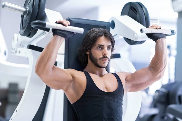 Fit adult bodybuilder working out with shoulder press machine in a gym during training in a healthy active lifestyle and fitness concept