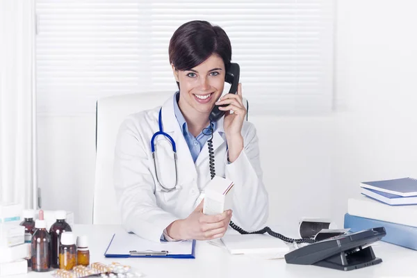 Усміхнена Молода Жінка Лікар Розмовляє Телефону Офісі Коли Вона Сидить — стокове фото