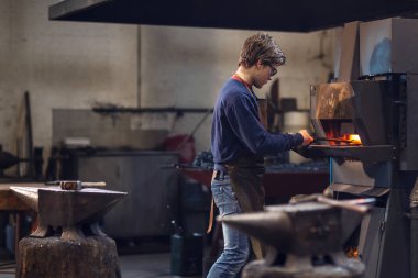 Ismarlama bir nesne üreten gibi maşa yakma fırını içinde bir dizi tutan bir metal işleme atölyede çalışan genç blaksmith