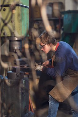 Genç blaksmith kırmızı sıcak metal bir atölye çalışmaları izlemek için öne eğilerek konsantrasyon ile uzman maşa kullanarak bir kalıp içinde holding ile çalışma