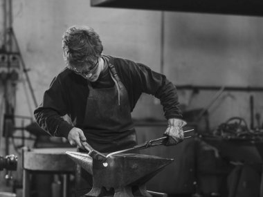 Genç metalworker veya kırmızı sıcak metal bir bobin bir çekiç örs üzerinde ile içine şekillendirme bir atölyede çalışan demirci