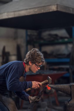 Genç metalworker veya kırmızı sıcak metal bir bobin bir çekiç örs üzerinde ile içine şekillendirme bir atölyede çalışan demirci