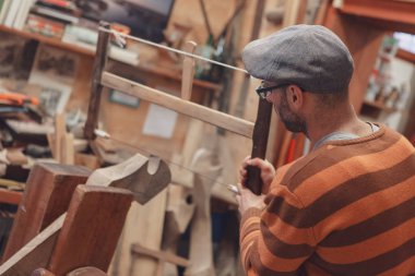 Eski moda kap ve soyulmuş kazak ahşap doğrama atölyesinde vintage ahşap yay testere aracı yandan görüntülendi ayrıntılarıyla testere marangoz