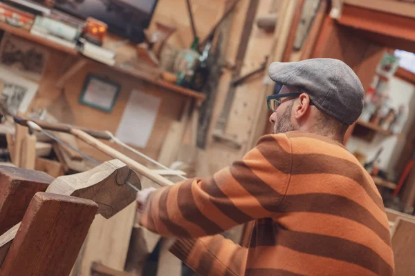 Eski moda kap ve soyulmuş kazak ahşap doğrama atölyesinde vintage ahşap yay testere aracı yandan görüntülendi ayrıntılarıyla testere marangoz